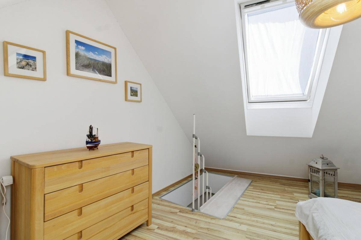 Gemütliches Schlafzimmer mit Holzboden, Kommode und einem Dachfenster, das viel Licht spendet.