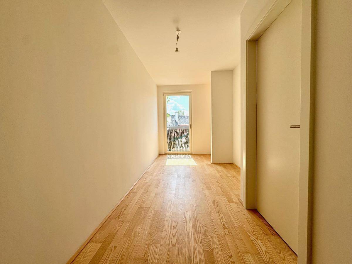 Heller, leerer Raum mit Holzboden und Zugang zu einem französischen Balkon, gut beleuchtet.