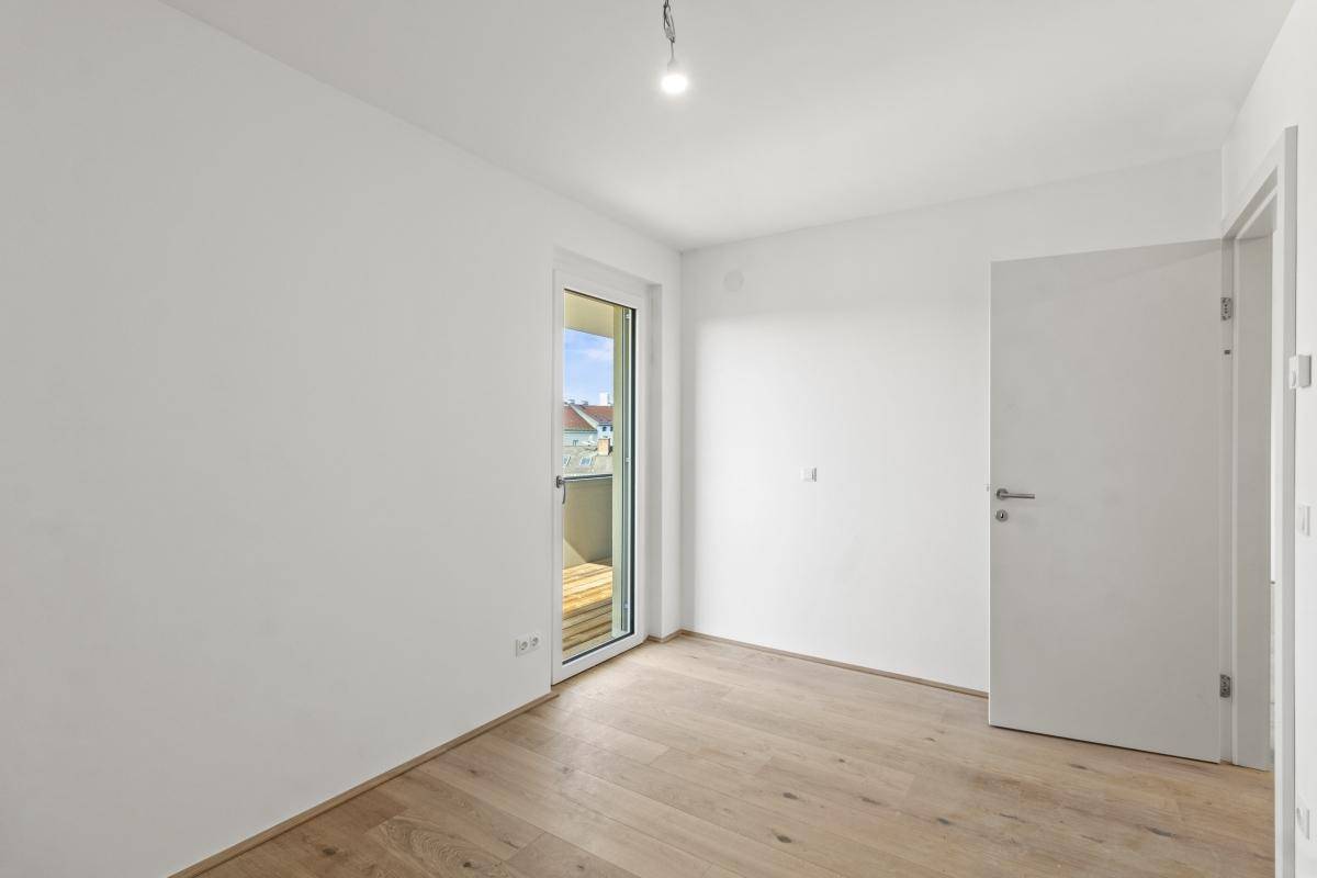 Helles Zimmer mit Holzboden und Tür, die zu einem Balkon führt.