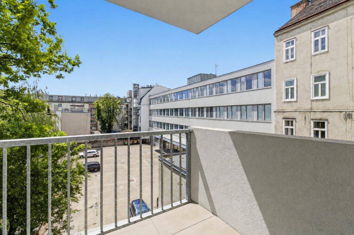 Balkon mit Blick auf den Innenhof und umliegende Gebäude unter blauem Himmel.