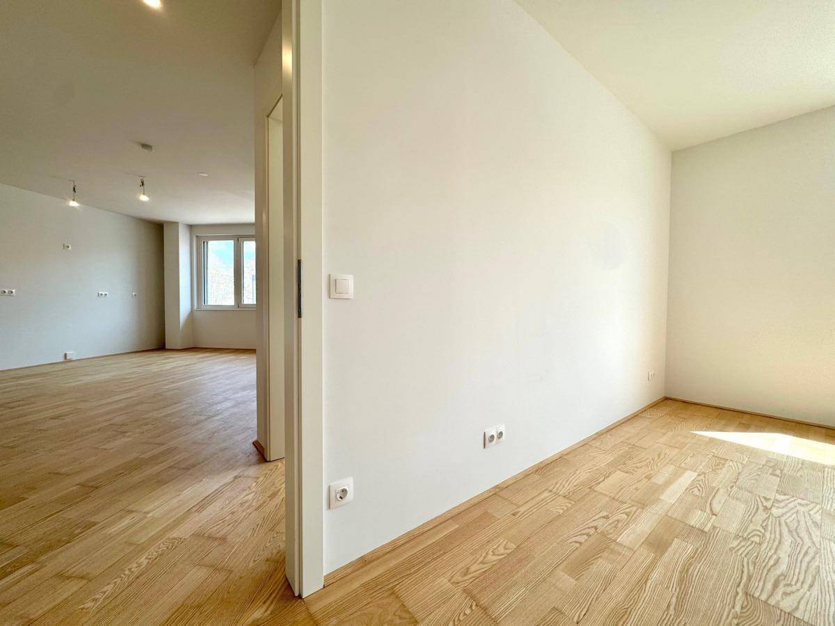 Blick aus einem Zimmer in den Flur, der zum hellen Wohnbereich mit Parkettboden führt.