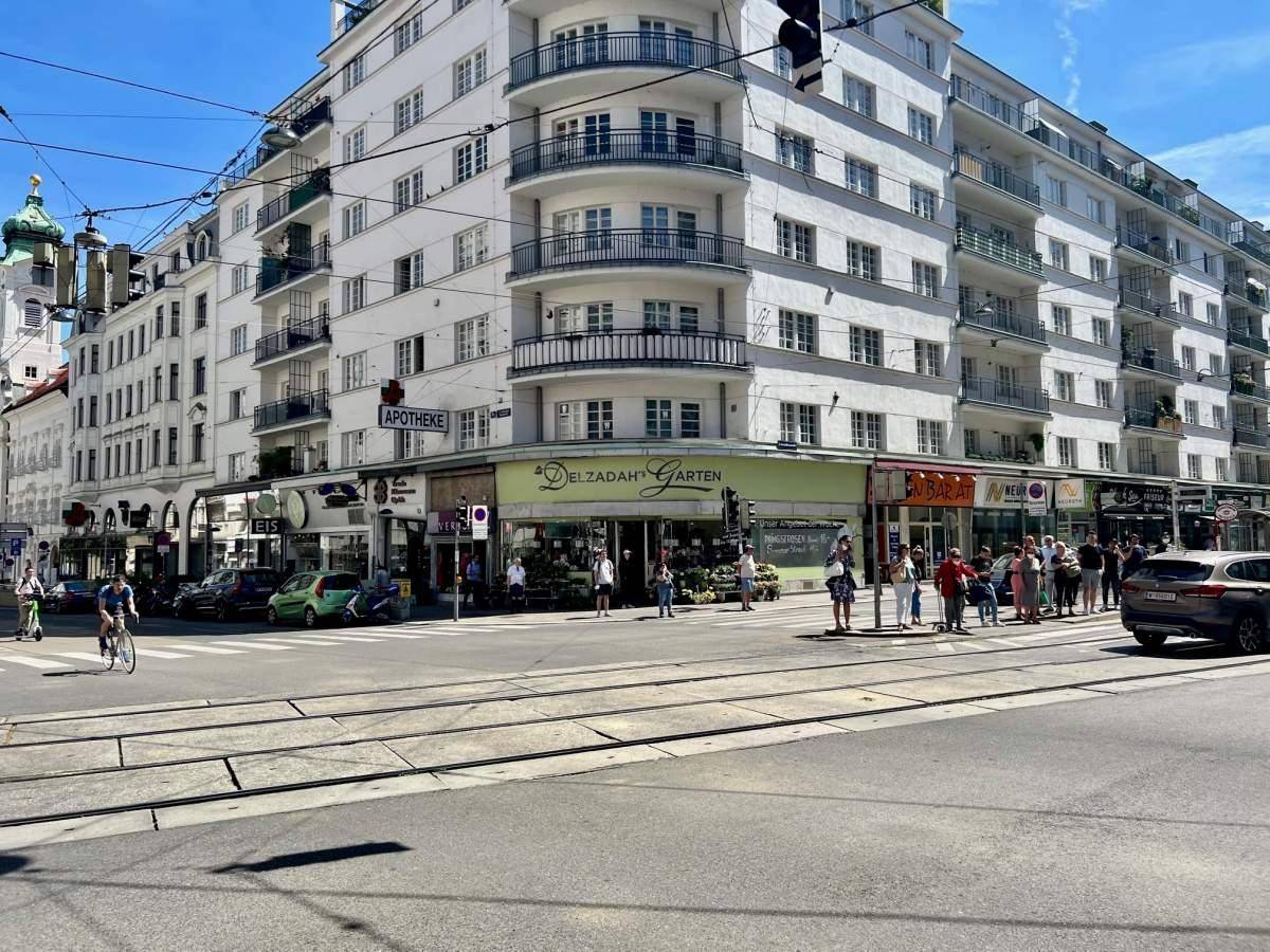 Eckgebäude in der Stadt mit Geschäften im Erdgeschoss und belebter Straßenkreuzung.