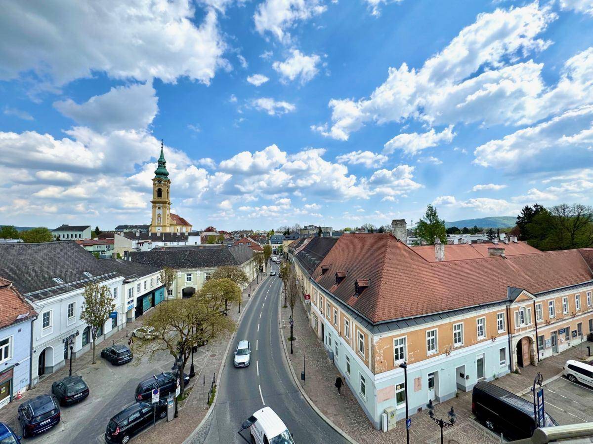 Weitläufiger Blick über die Dächer der Stadt mit einem Kirchturm und grünen Hügeln im Hintergrund.