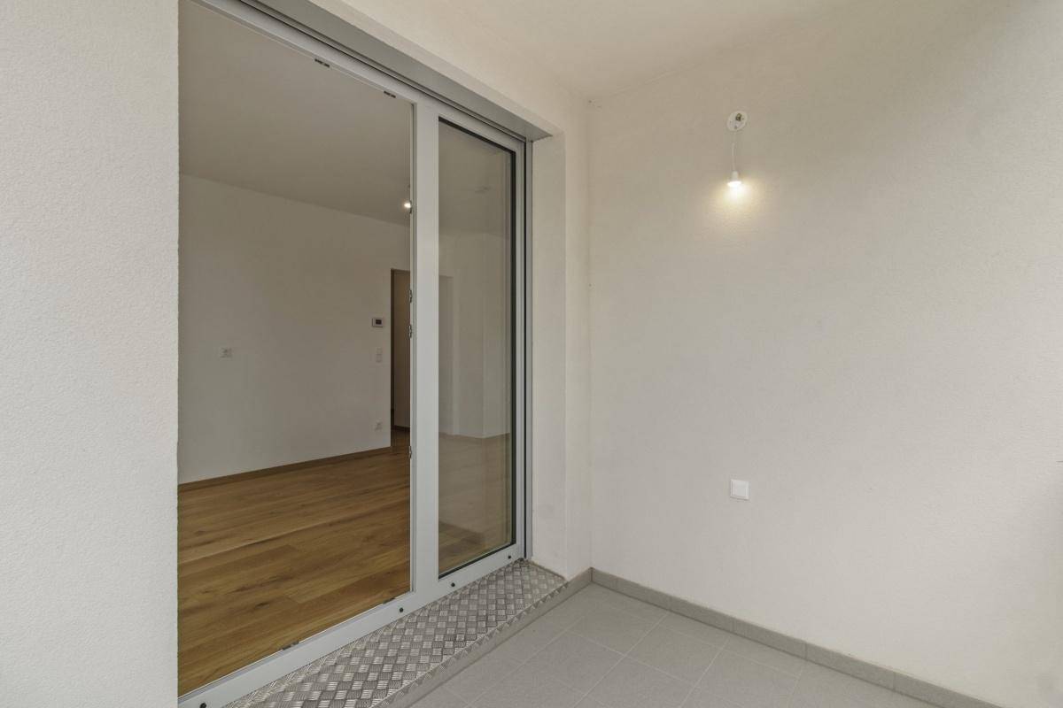 Heller Balkon mit Schiebetür zum Innenraum und Fliesenboden, bereit zur Nutzung.