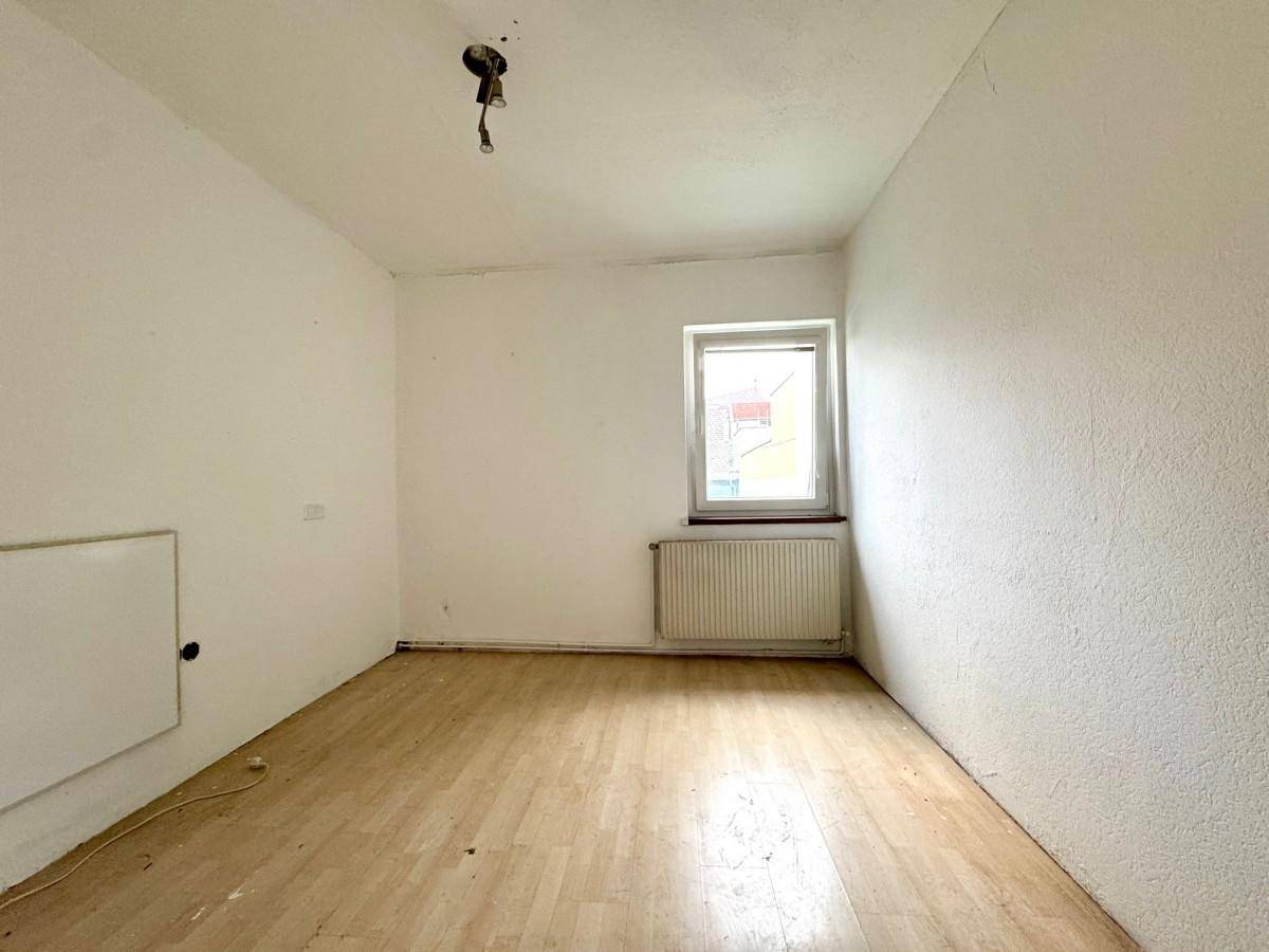 Helles Zimmer mit Holzboden, Fenster und Heizkörper unter dem Fenster.