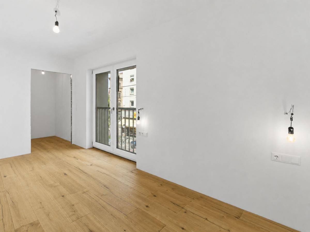 Leerer Raum mit Holzparkett, französischem Balkon und Zugang zu einem weiteren Zimmer.