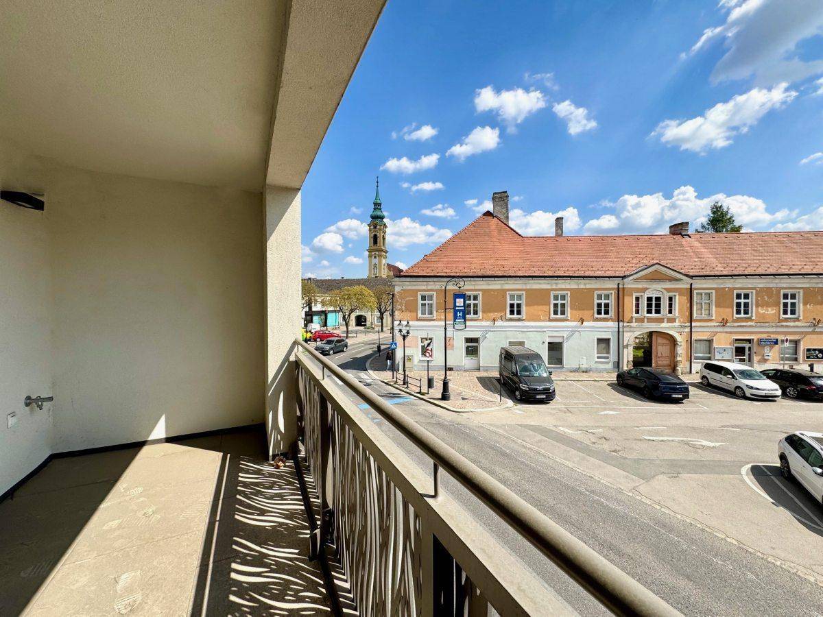 Heller Balkon mit Blick auf den belebten Stadtplatz und historische Gebäude.