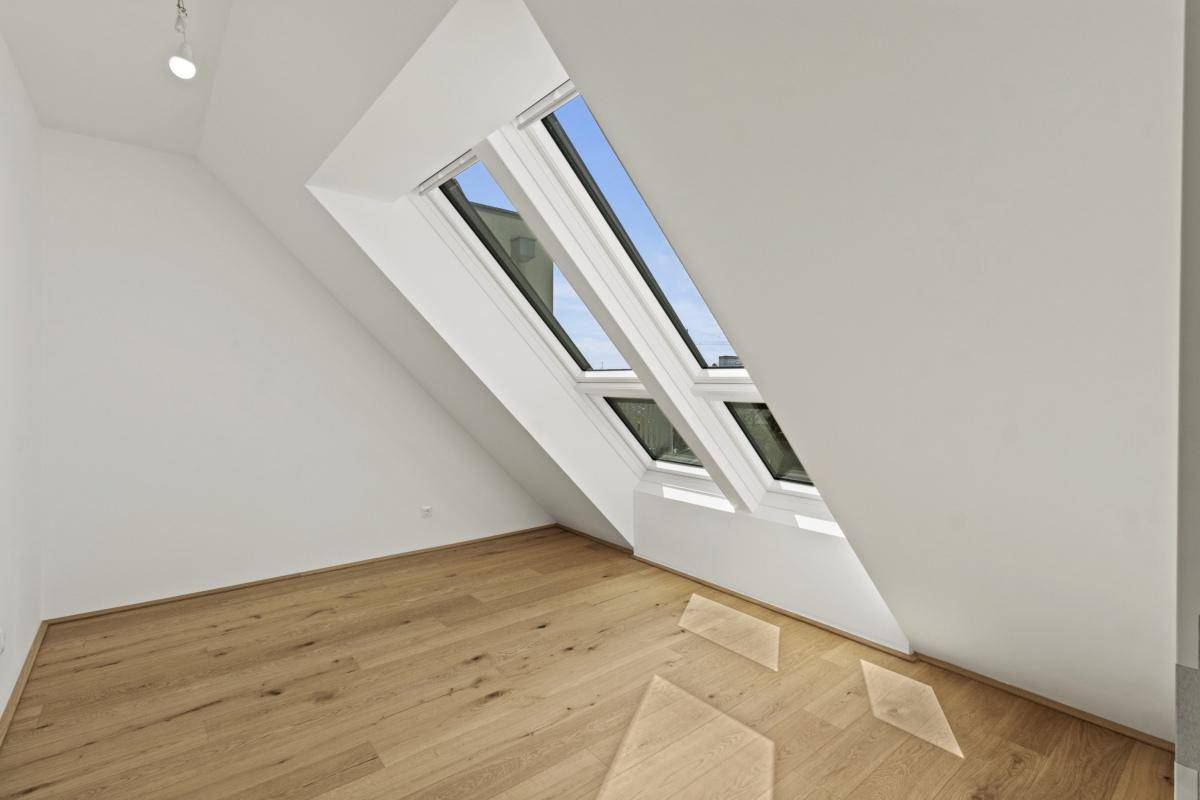 Leerer Dachgeschossraum mit Holzboden und schrägen Dachfenstern, sehr hell und einladend.