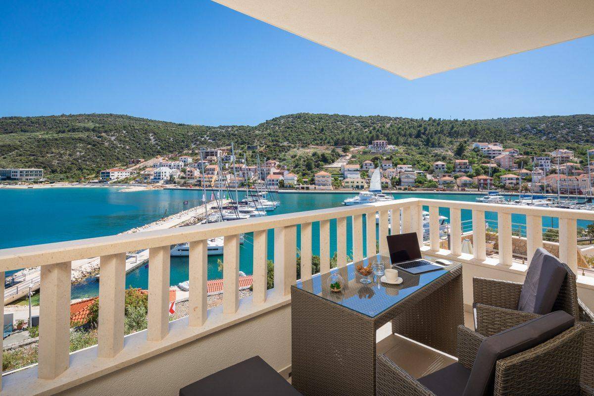 Möblierter Balkon mit Rattanmöbeln und atemberaubendem Blick auf den Hafen und das azurblaue Meer.