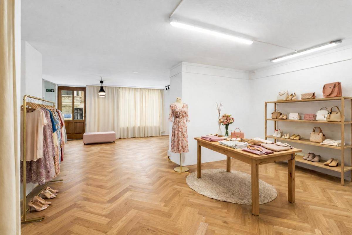 Heller Verkaufsraum mit Fischgrätparkett, modernen Kleiderständern und Regalen für Accessoires, gut beleuchtet.