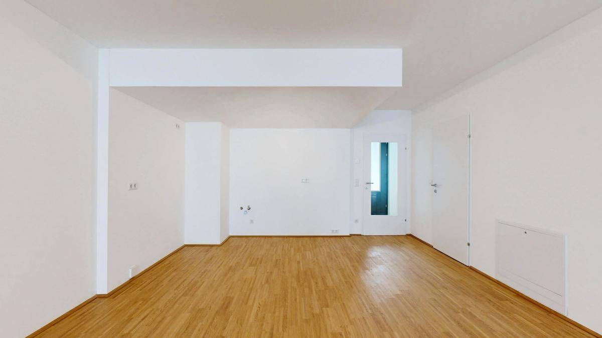 Heller, leerer Wohnraum mit Parkettboden und weiß gestrichenen Wänden.