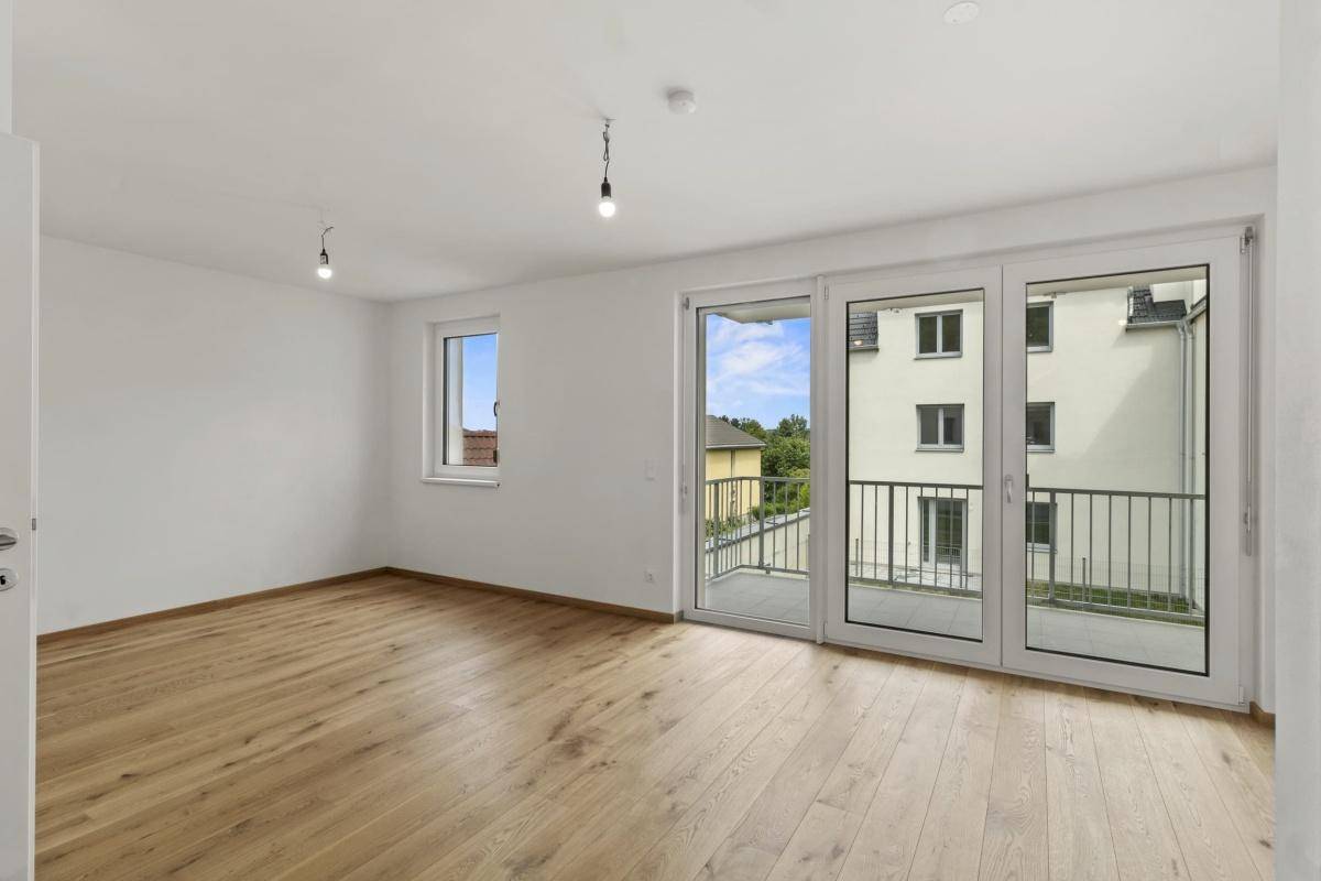 Helles Wohnzimmer mit Eichenparkettboden und Zugang zu einem Balkon.