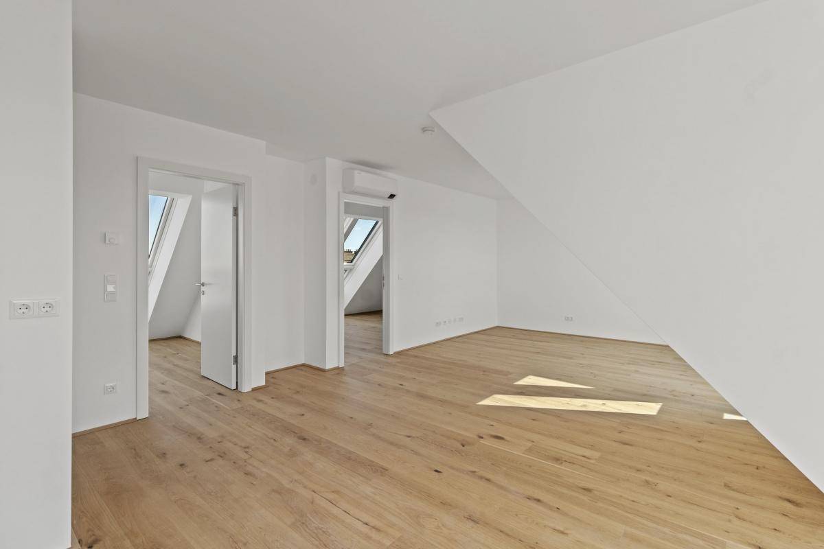 Geräumiger, heller Raum im Dachgeschoss mit Holzboden, schrägen Wänden und mehreren Türen.