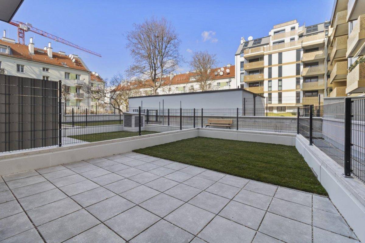 Gepflasterte Terrasse mit kleiner Rasenfläche und Blick auf die umliegenden Gebäude.