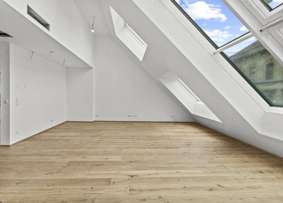 Lichtdurchfluteter Raum mit Holzboden und schrägen Wänden, ausgestattet mit mehreren Dachfenstern.