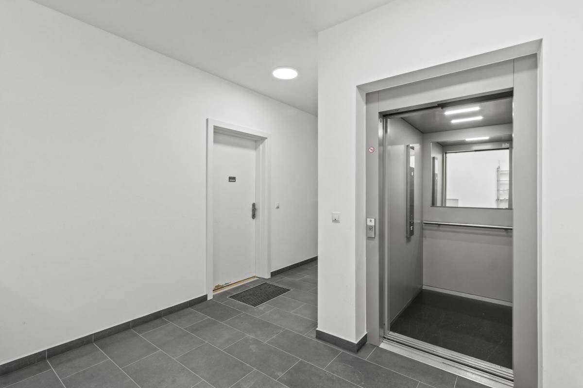 Heller Flur im Gebäude mit grauen Bodenfliesen und einem modernen Aufzug für bequemen Zugang.