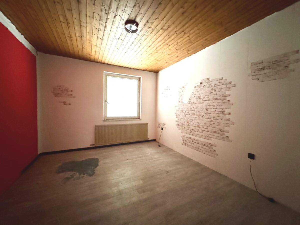 Leerer Raum mit Holzdecke, einem Fenster und teilweise freigelegten Ziegelwänden.