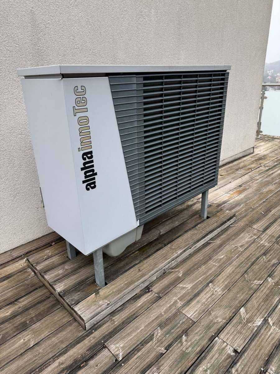 Eine Alpha InnoTec Wärmepumpe steht auf einer Holzterrasse, Teil der Haustechnik.