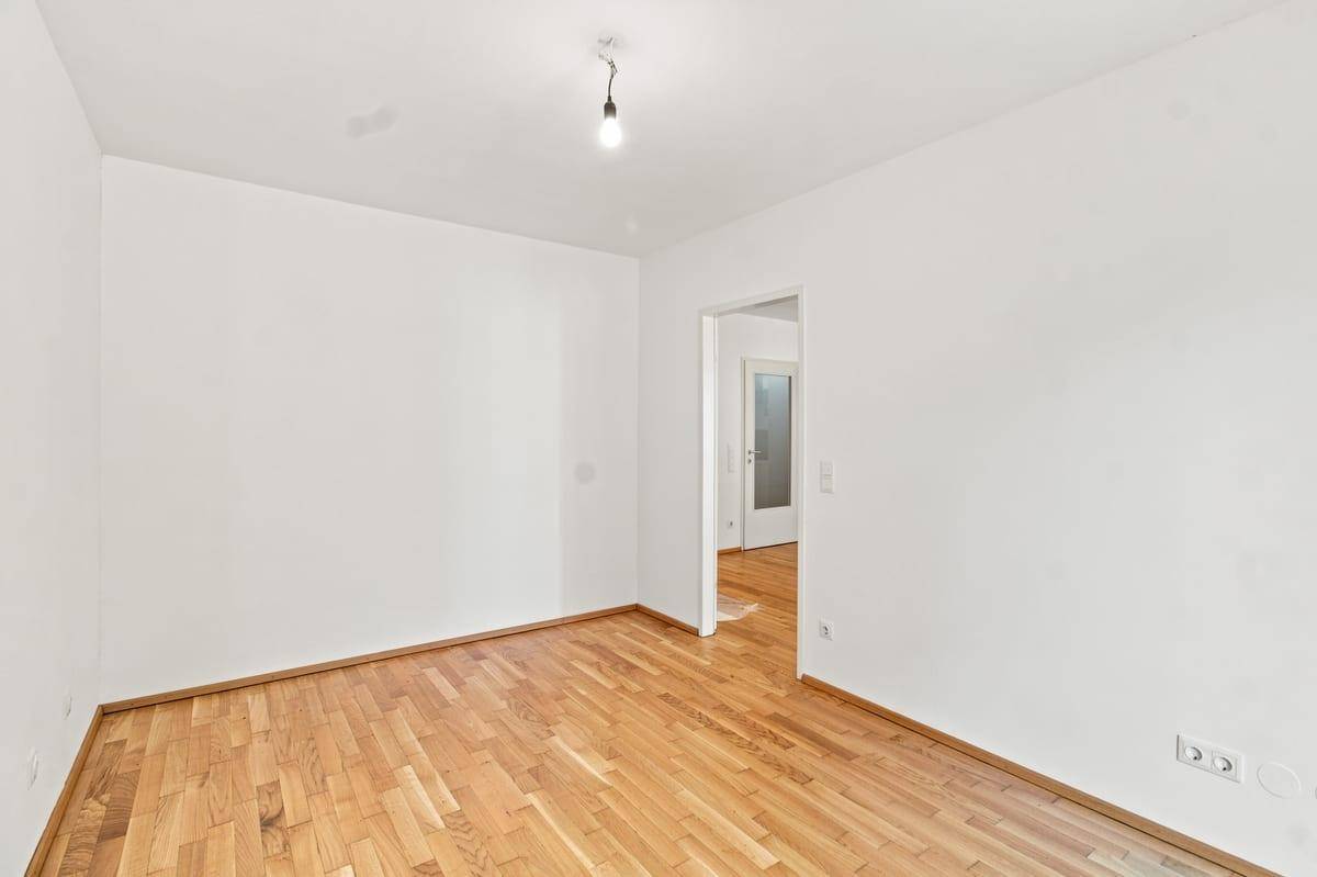 Leerer Raum mit Holzboden und weißen Wänden, ideal für individuelle Gestaltung.