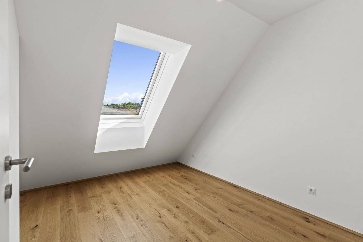 Heller Raum im Dachgeschoss mit Holzboden, Dachschräge und großem Dachfenster.