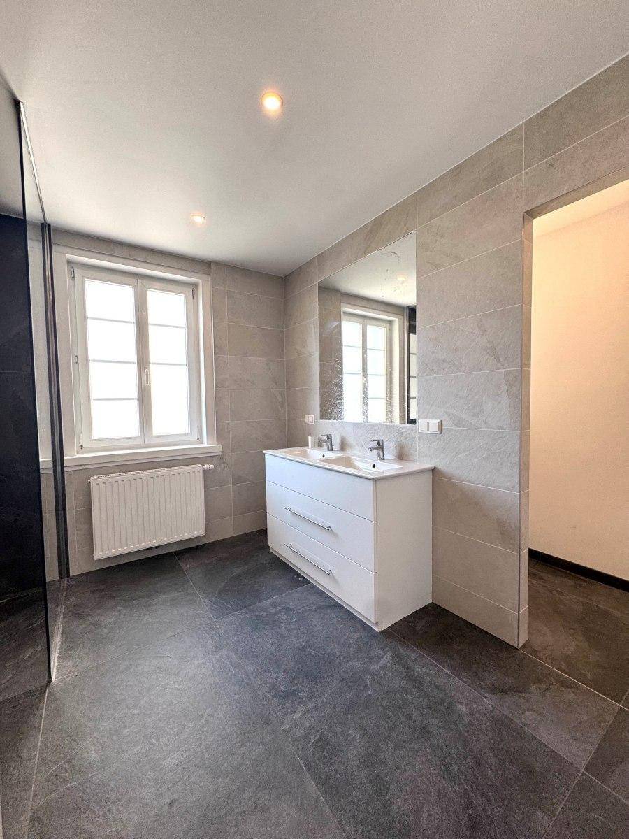 Modernes Badezimmer mit grauen Fliesen, Doppelwaschbecken und großem Spiegel, hell und geräumig.