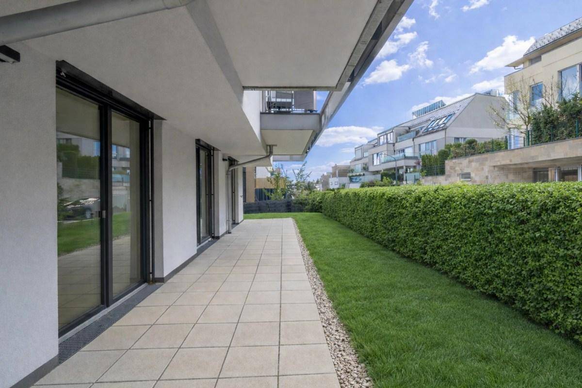 Lange gepflasterte Terrasse mit angrenzendem Rasen und einer hohen Hecke.