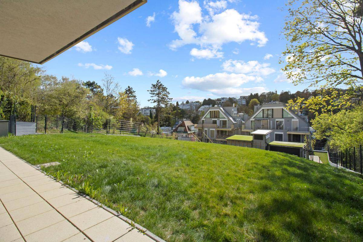 Weitläufige Terrasse mit Panoramablick über eine grüne Wiese und die benachbarten Häuser.