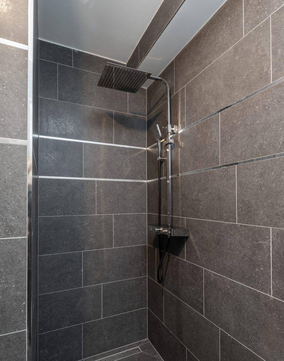 Moderne Dusche mit Regenduschkopf und dunklen großformatigen Fliesen.