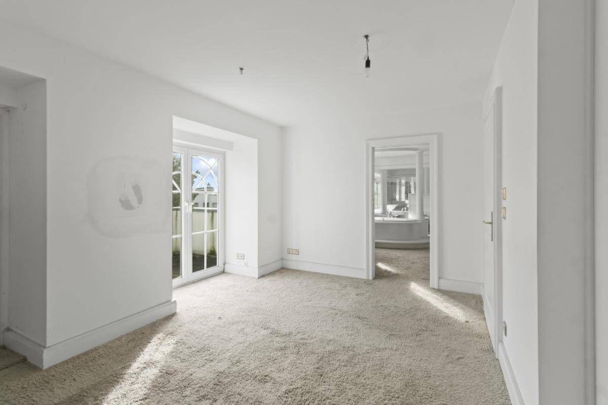 Leeres Zimmer mit Teppichboden und Zugang zu einem Balkon oder einer kleinen Terrasse.