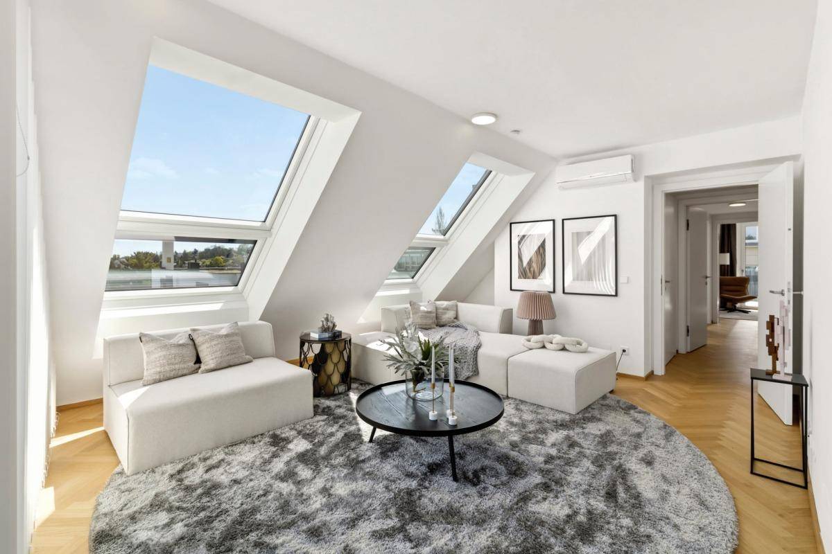 Helles Wohnzimmer mit modernem Sofa, rundem Teppich und großen Dachfenstern.