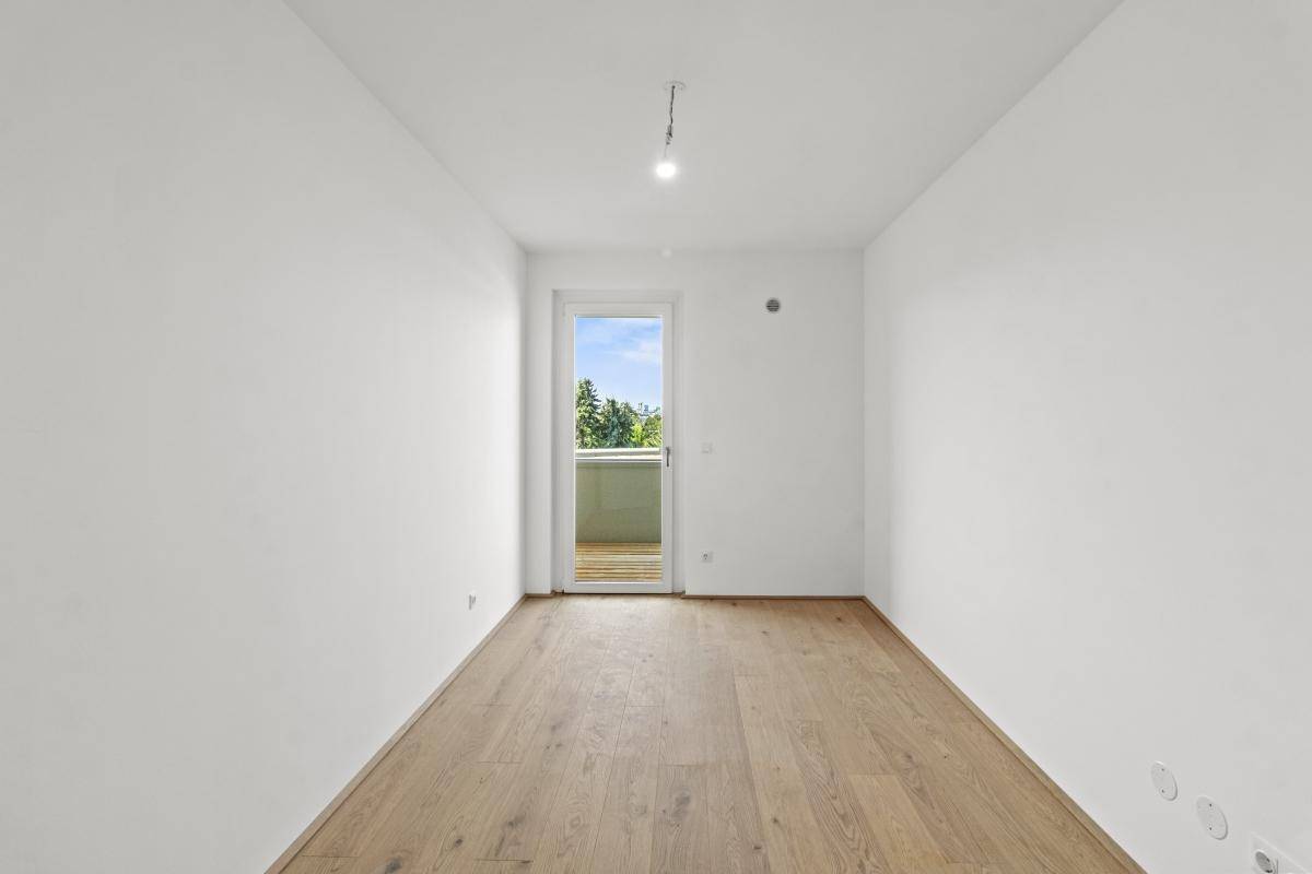 Lichtdurchflutetes Zimmer mit Holzboden und Zugang zu einem kleinen Außenbereich.