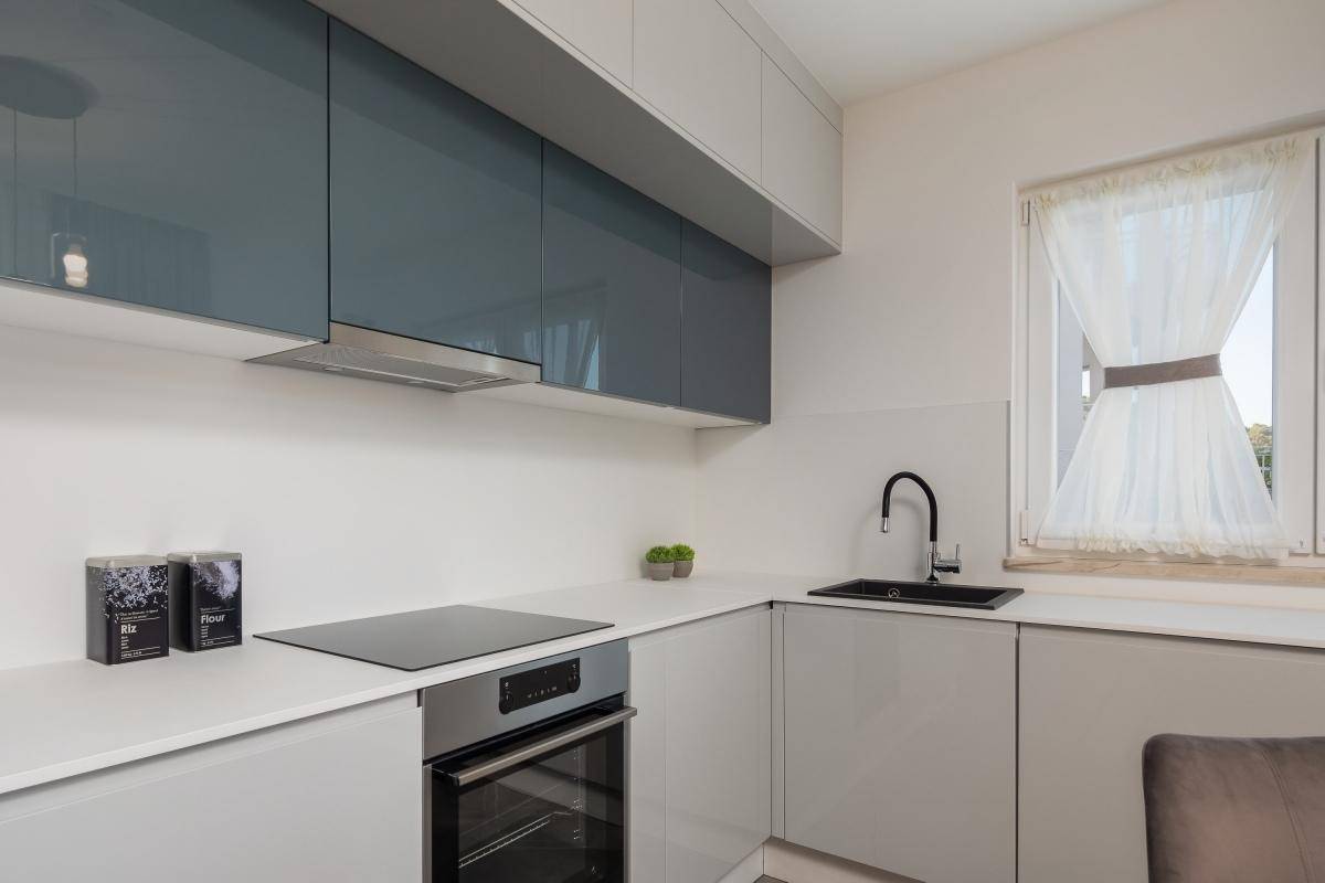 Funktionale, moderne Küche mit grauen und blauen Schränken, Induktionskochfeld und Backofen.