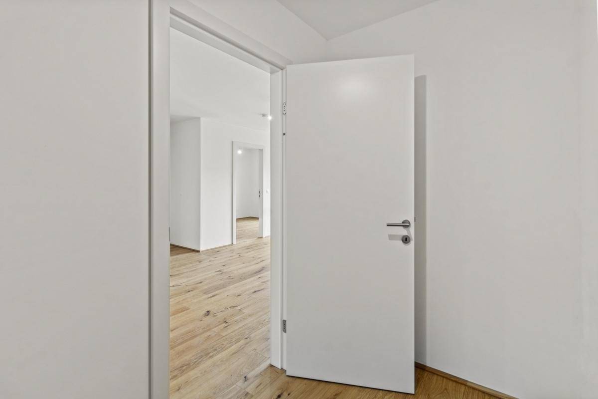 Offene weiße Tür führt in einen hellen Raum mit Holzboden und klaren Linien.