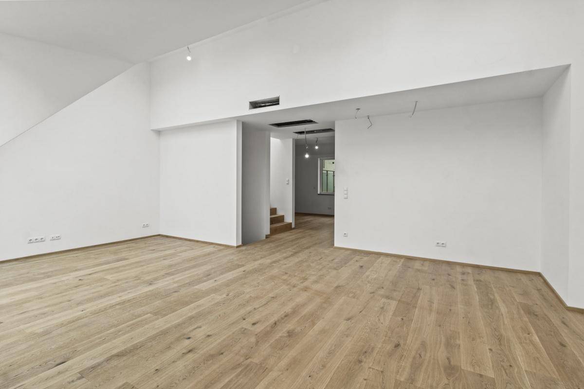 Offener Wohnbereich mit Holzboden und weißen Wänden, der in einen weiteren Raum übergeht.