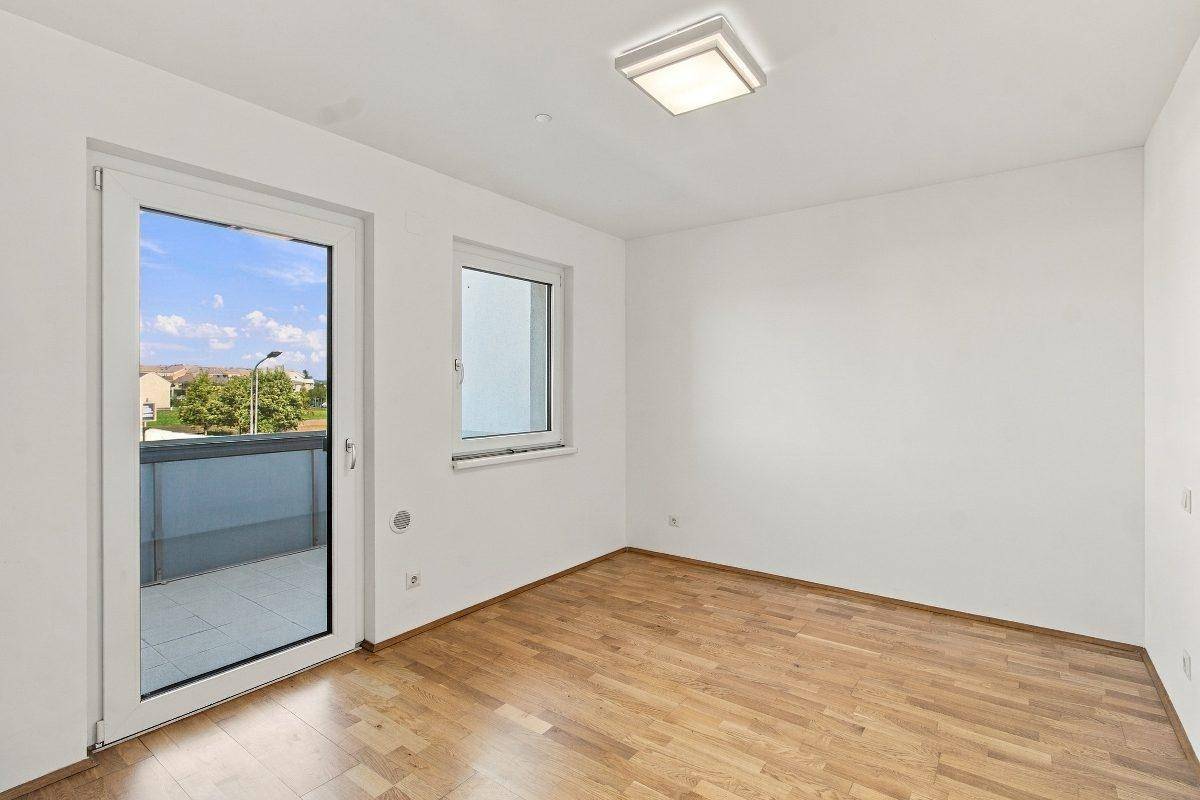 Leeres Schlafzimmer mit Holzboden und Balkontür, ideal für individuelle Einrichtung.