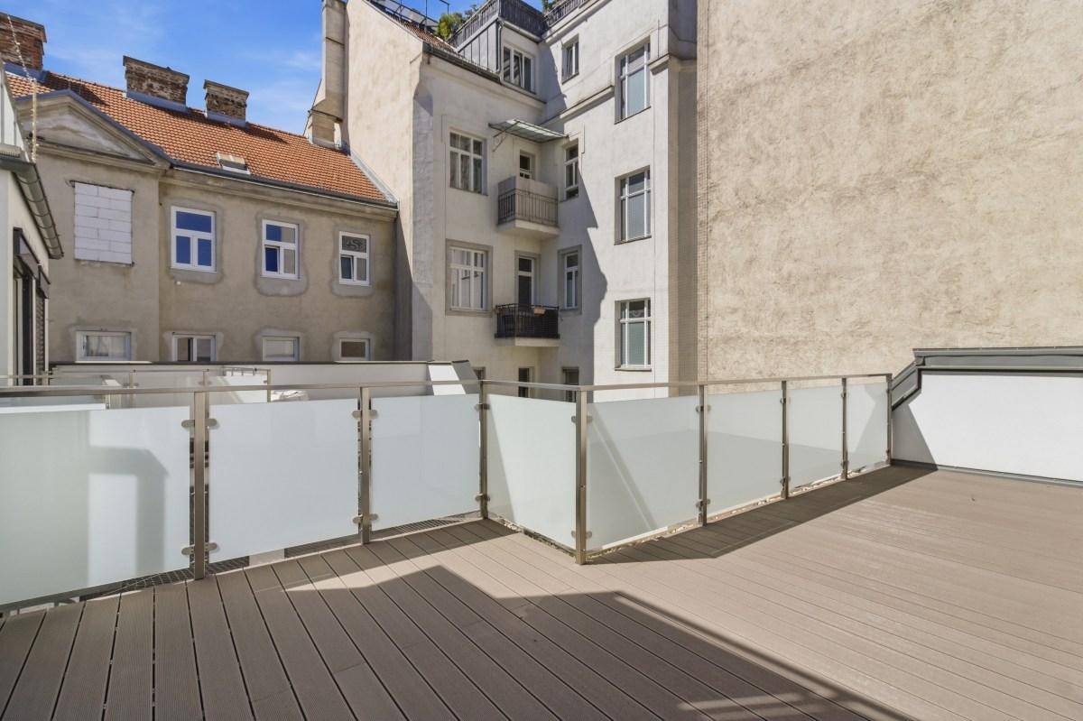 Weitläufige Dachterrasse mit modernem Glasgeländer und Blick auf die umliegenden Gebäude.