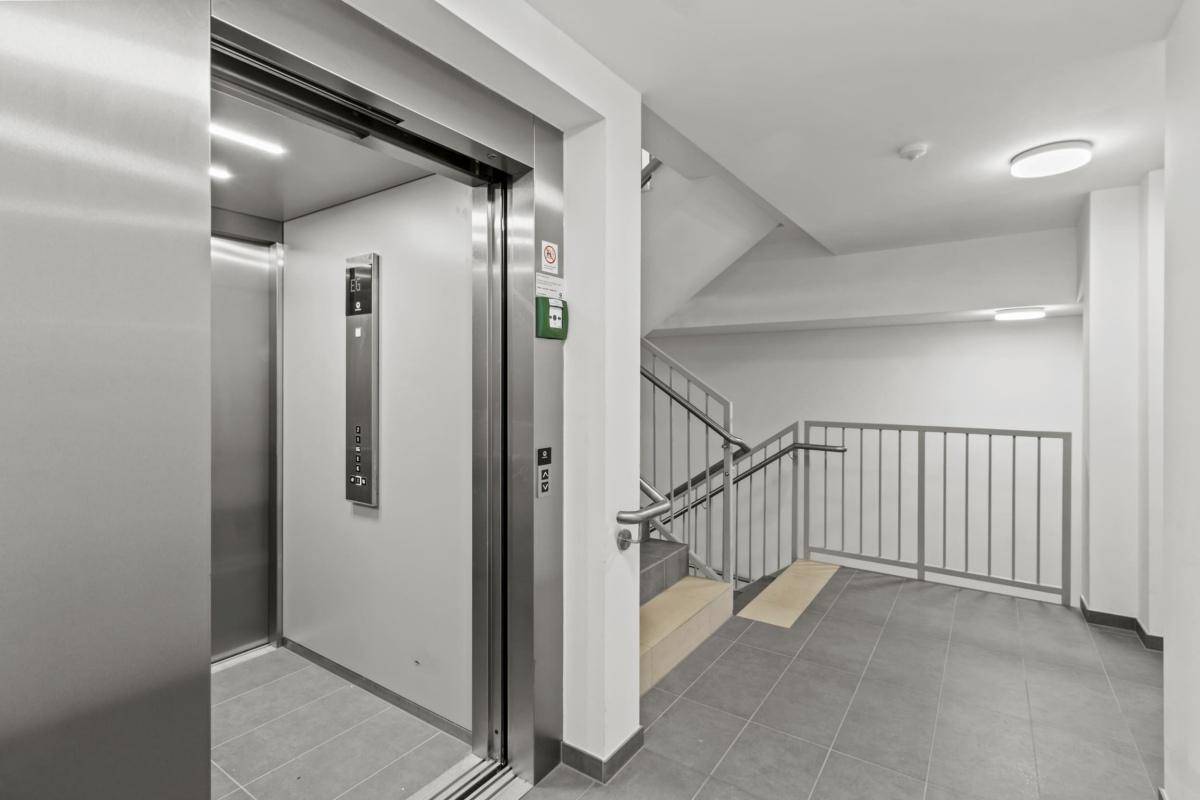 Heller Eingangsbereich mit Aufzug und Treppenhaus, ausgestattet mit Fliesenboden und Metallgeländer.