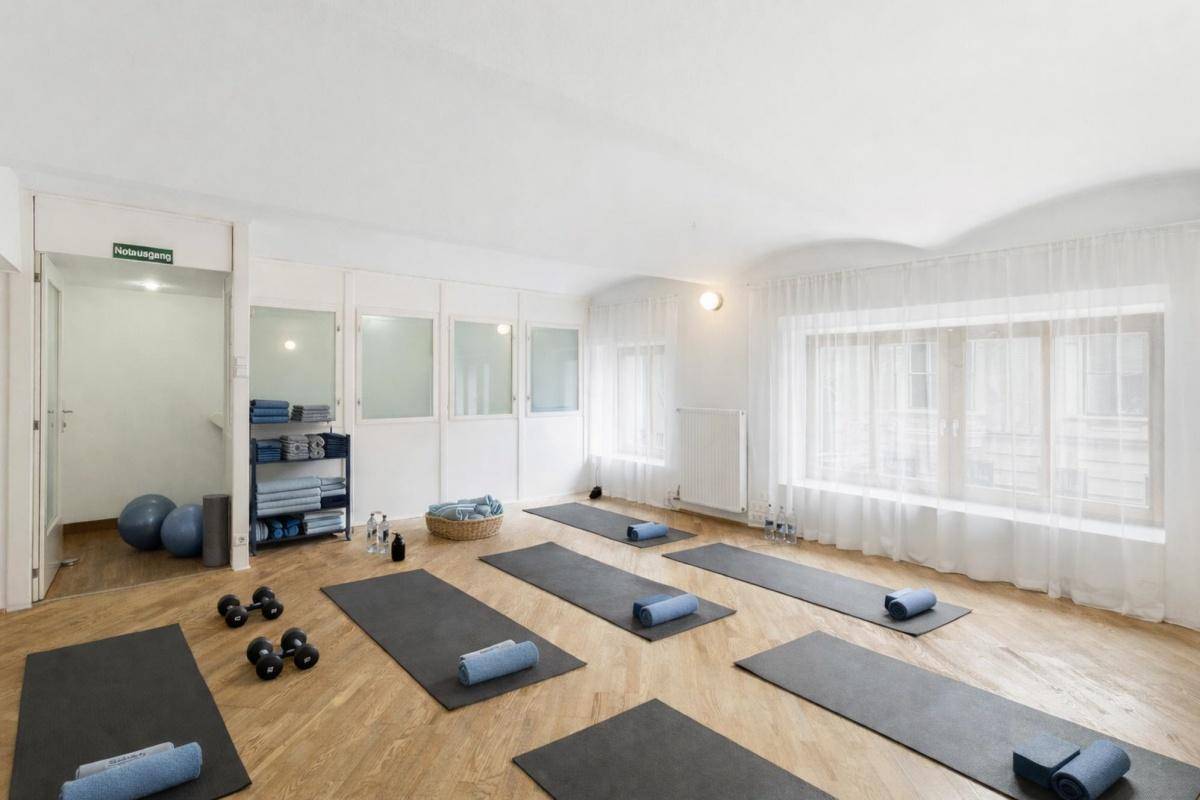 Geräumiger Fitnessraum mit Yogamatten, Hanteln und großen Fenstern für natürliches Licht, ideal für Kurse.