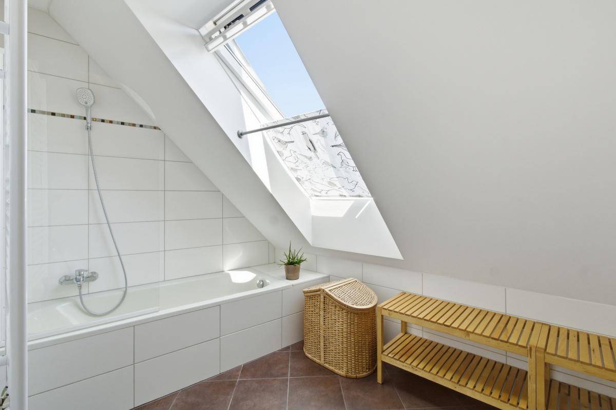 Modernes Badezimmer mit Badewanne, weißen Fliesen und einem Dachfenster für natürliches Licht.