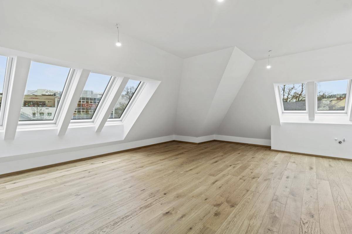 Lichtdurchflutetes Dachgeschosszimmer mit Holzboden und mehreren Dachfenstern in einem Neubau.
