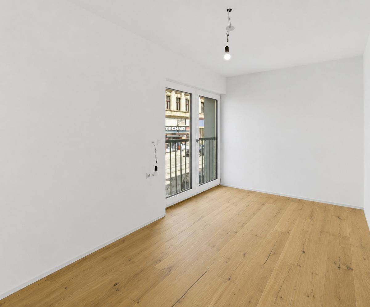 Unmöblierter Raum mit Holzboden und Fenster mit Blick auf die belebte Straße.