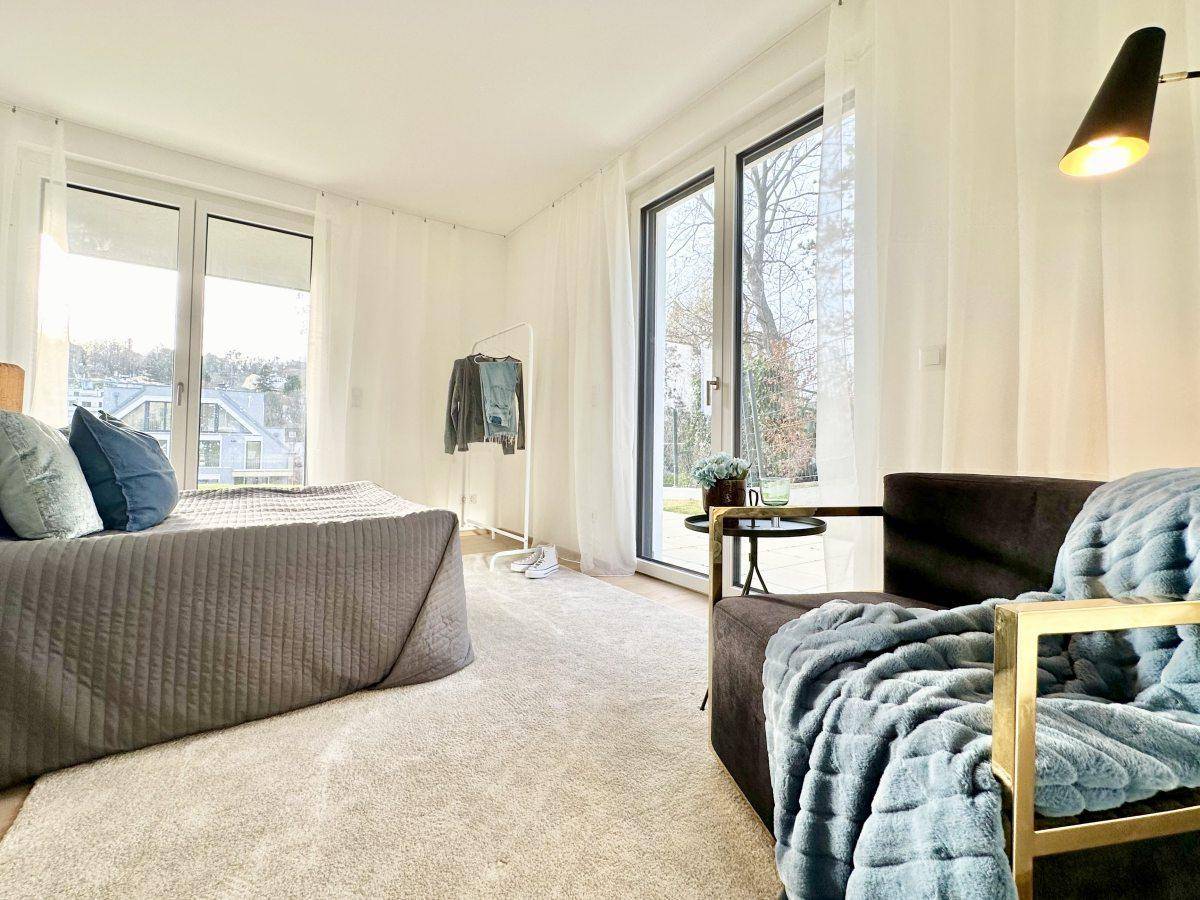 Komfortables Schlafzimmer mit Bett, Sessel und großen Fenstern, die viel Licht hereinlassen.
