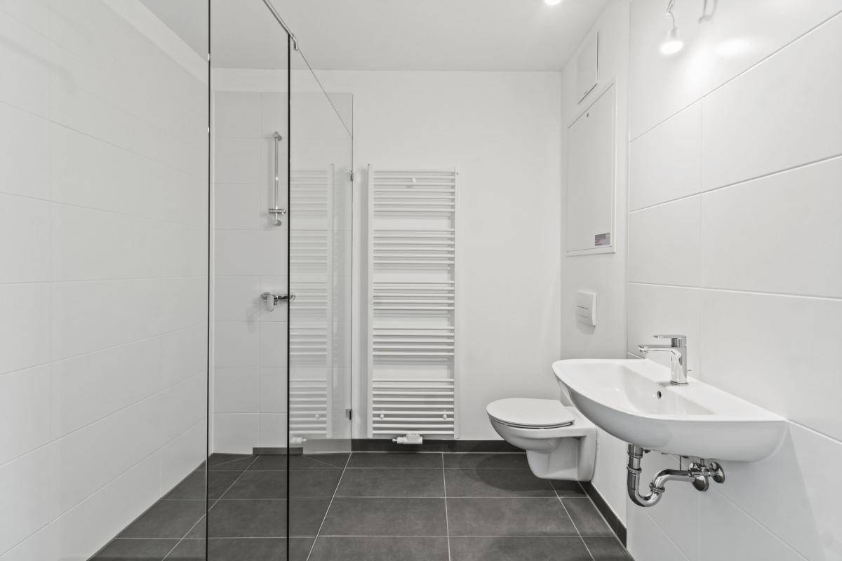 Modernes Badezimmer mit ebenerdiger Dusche, dunklen Fliesen und beheiztem Handtuchhalter.