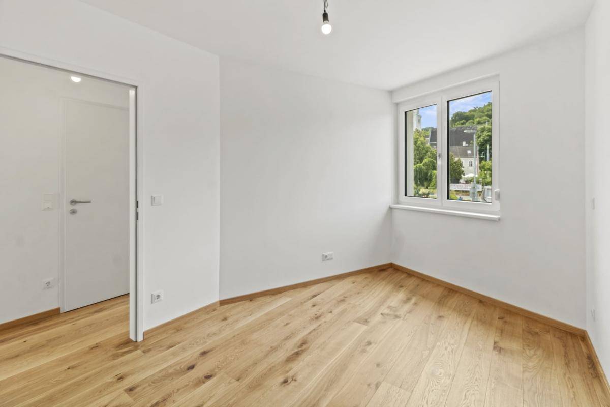 Helles Schlafzimmer mit Parkettboden und Fenster mit Blick auf grüne Hügel.
