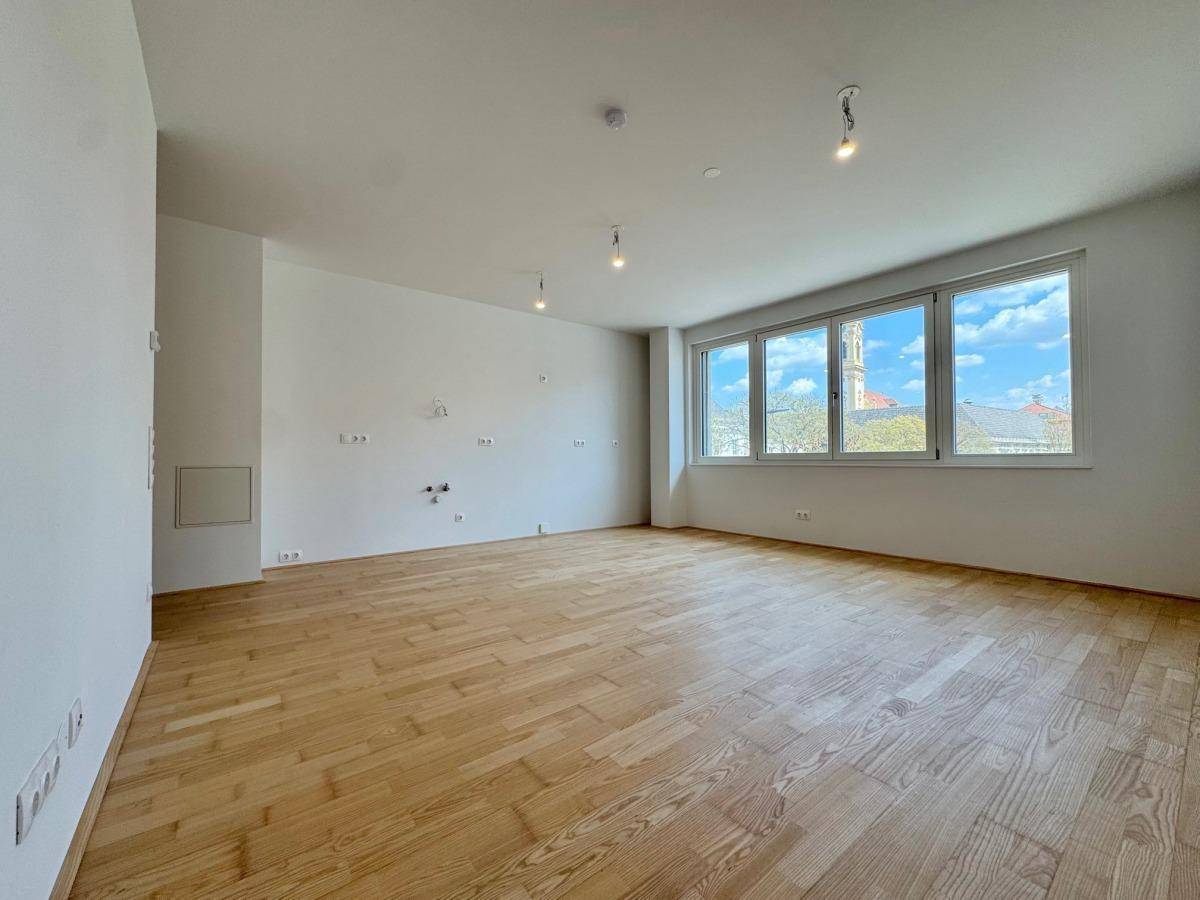 Geräumiges Wohnzimmer mit hellem Parkettboden und Blick auf die Stadt durch die Fenster.