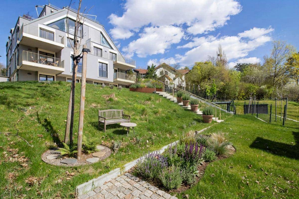 Modernes Mehrfamilienhaus mit gestuften Balkonen und begrünter Hanglage unter blauem Himmel.