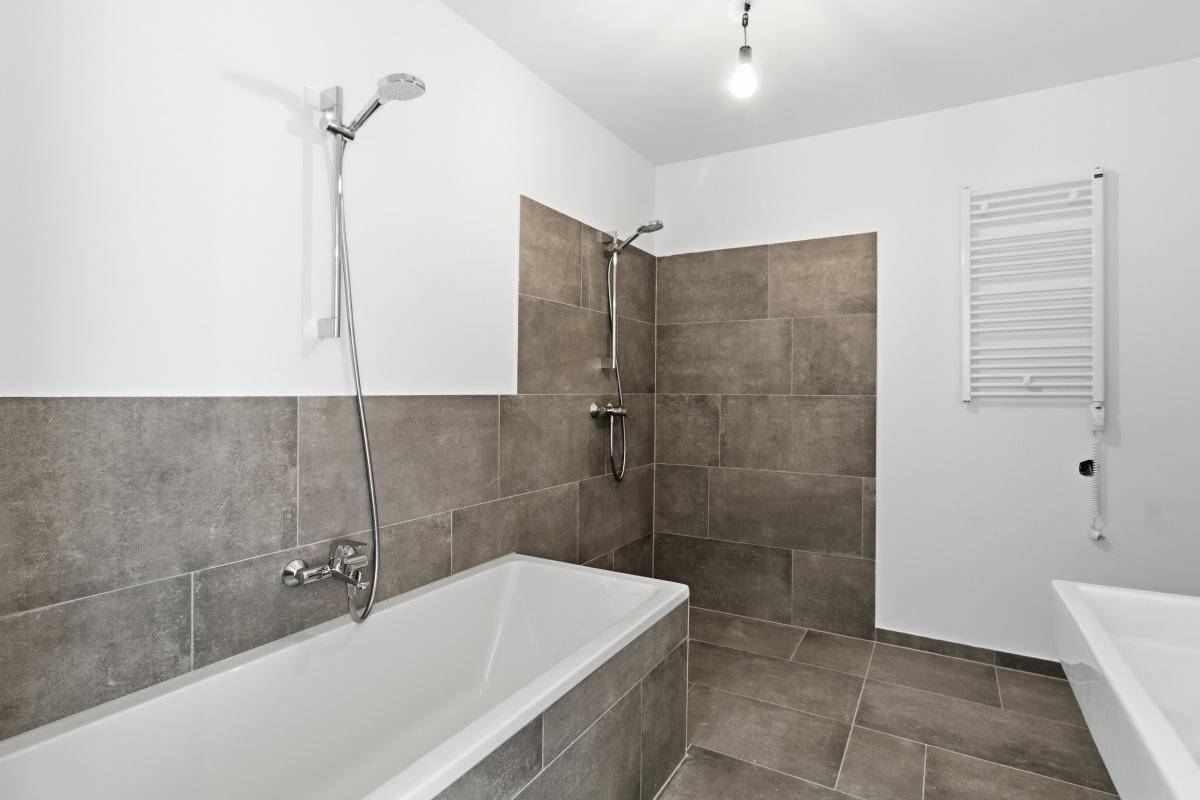 Modernes Badezimmer mit grauen Fliesen, Badewanne mit Duschfunktion und beheiztem Handtuchhalter.