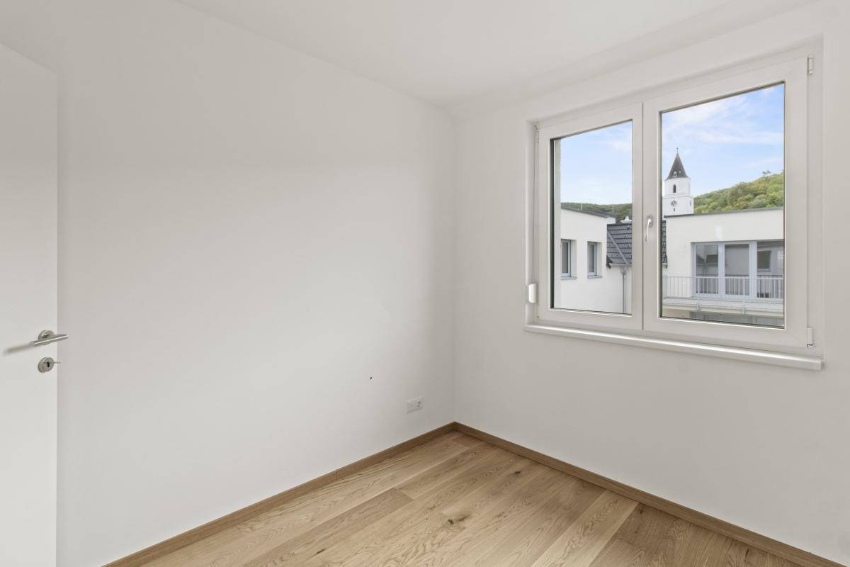 Leeres Schlafzimmer mit Holzboden, weißen Wänden und einem Fenster mit Blick auf die Umgebung.