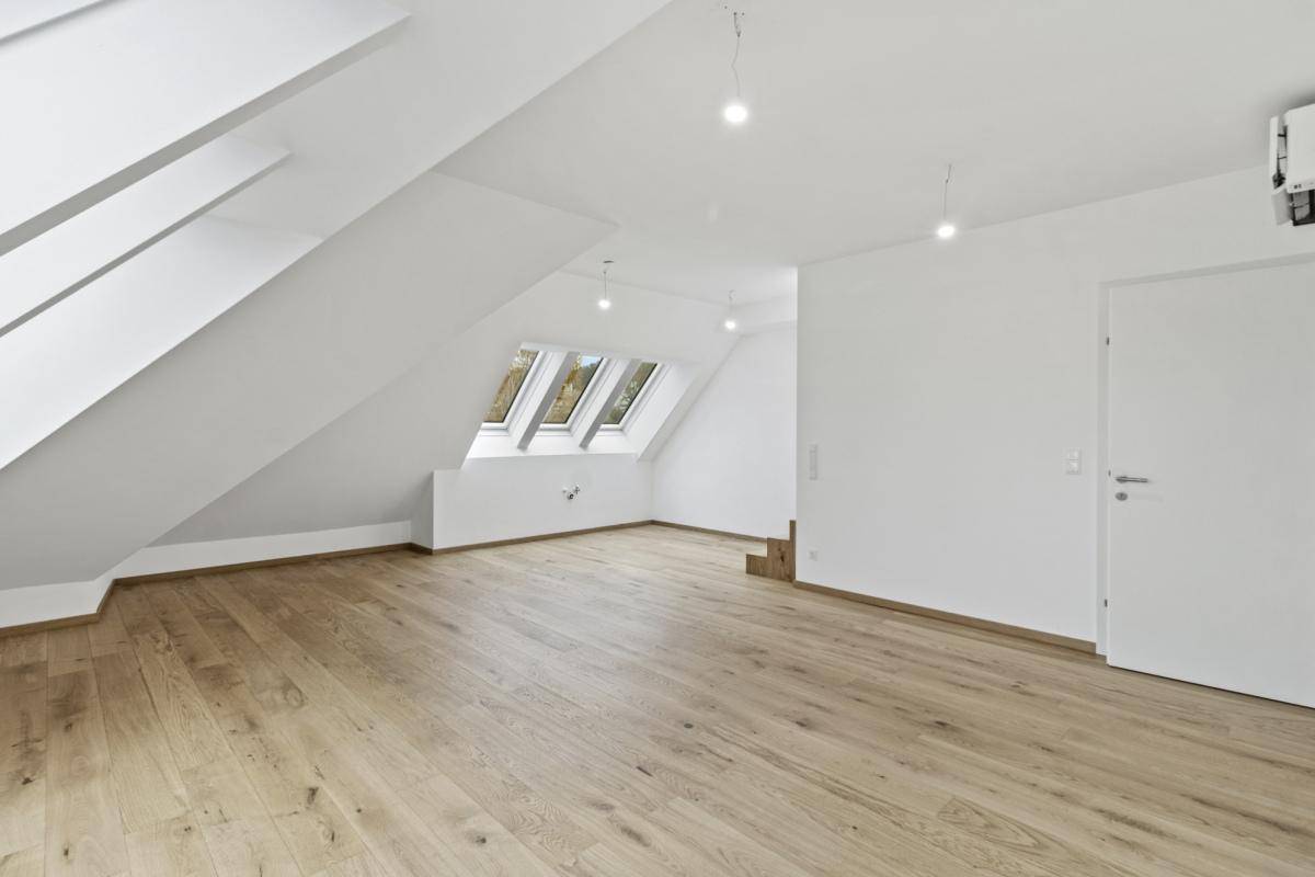 Weitläufiges Dachzimmer mit Holzboden, Dachfenstern und Zugang zu weiteren Räumen im Dachgeschoss.
