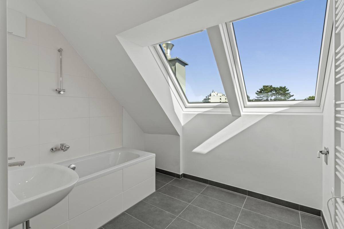 Modernes Badezimmer mit Badewanne, grauen Fliesen und großem Dachfenster.